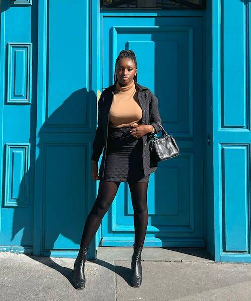 Femme brune portant une jupe noire, un col roulé et un manteau fabriqués en France à Paris.