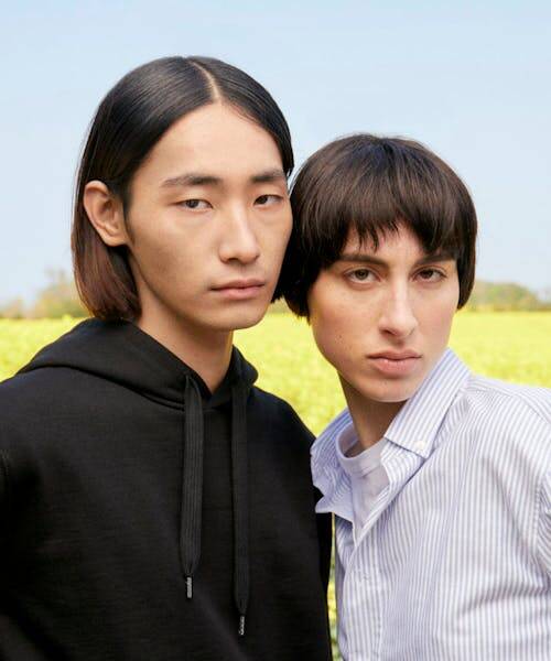 Le vestiaire mixte fabriqué en France. Homme portant un sweat noir et une femme portant une chemise blanche à rayures verticales grises.