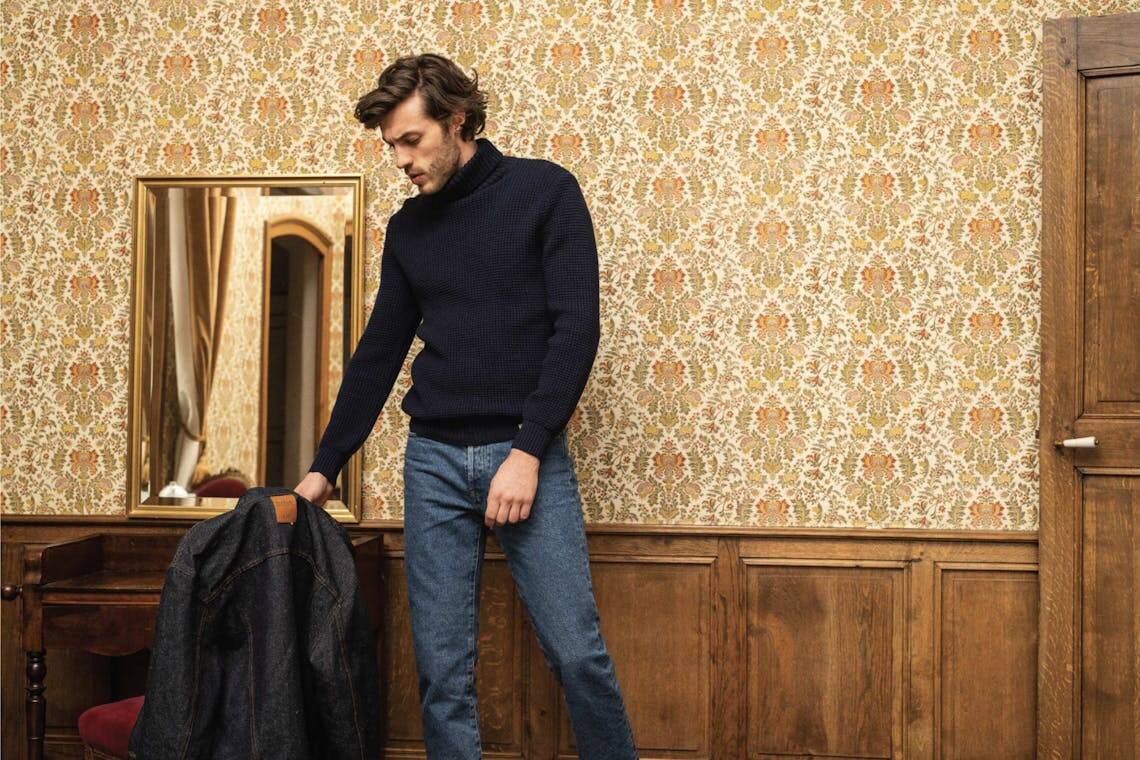 Homme dans un salon portant un jean brut fabriqué en France, un col roulé et une veste en jean.