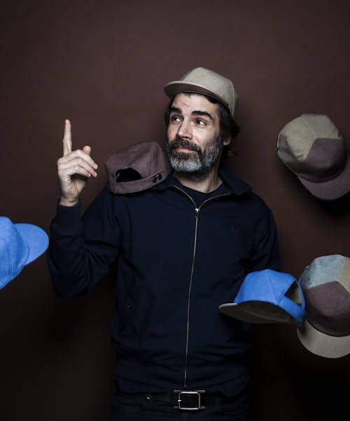 Homme brun portant et entouré de casquettes fabriquées en France par le Panache Paris.