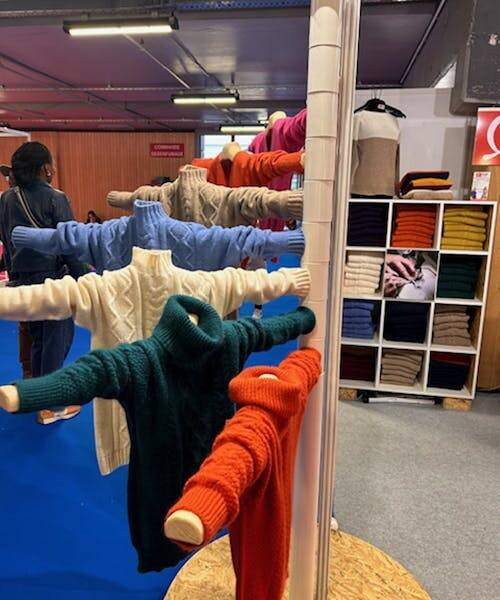 Exposition de pulls made in France aux multiples couleurs : orange, vert, blanc, bleu, beige et rose.