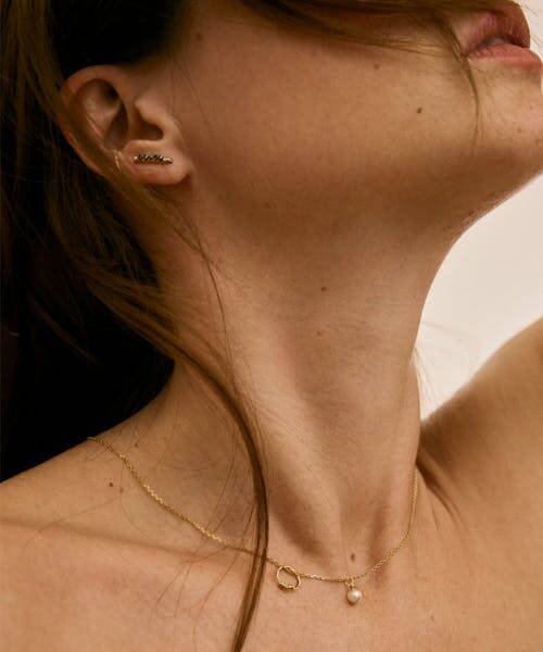 Femme brune portant un collier dorée avec un anneau et une perle.