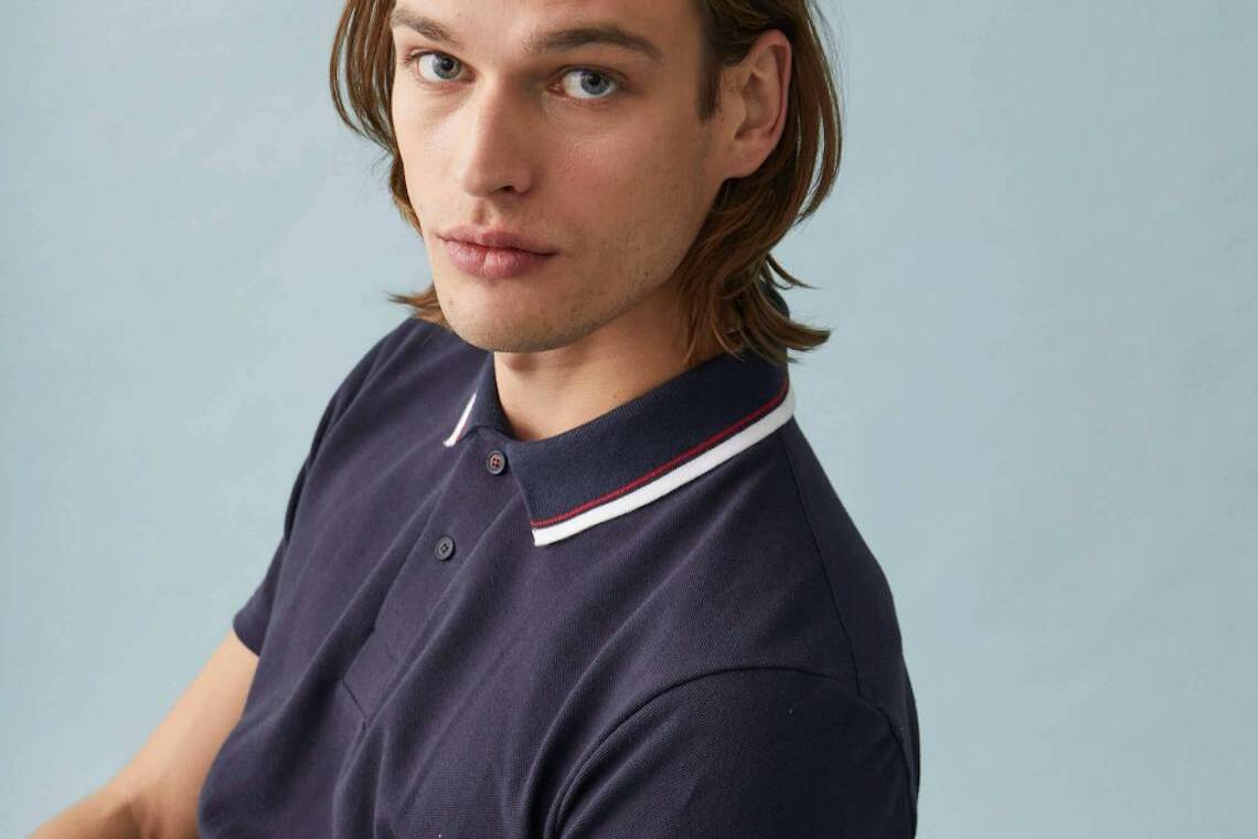 Homme aux cheveux mi-long portant un polo bleu fabriqué en France par Le Slip Français.