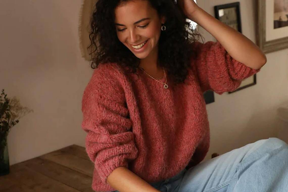 Femme portant un pull rose flash fabriqué en France à Clamart et un jean bleu clair.