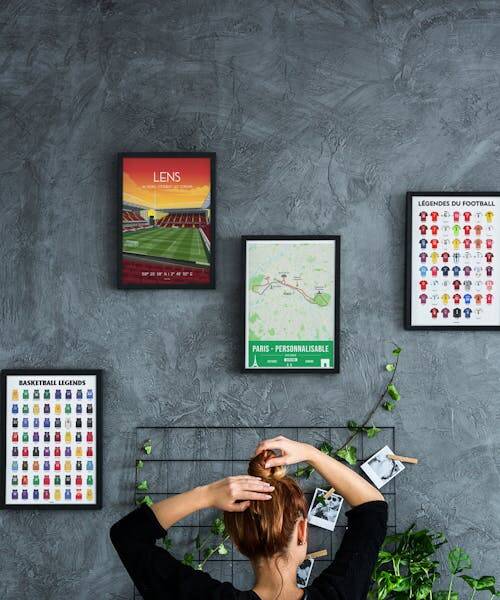 Femme devant un mur décorés de posters fabriqué en France :  un poster avec les légendes du basketball, un autre avec les légendes du football et une affiche du RC Lens.