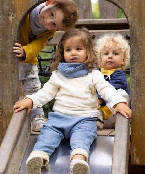 Trois enfants en haut d'un toboggan habillé avec des vêtements fabriqués en France par Petit Pote.