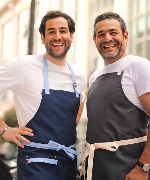 Deux cuisiniers portant un tablier bleu et un tablier gris fabriqués en France par Atelier TB.