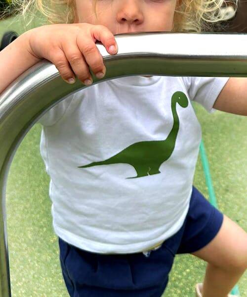 Enfant portant un t-shirt blanc avec un dessin d'un Diplodocus fabriqué en France.