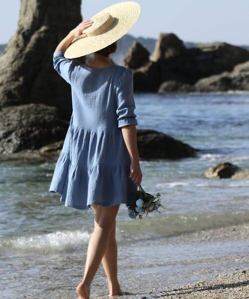 Femme marchant sur la plage portant un chapeau et une robe bleu Made in France de Pantaïa.