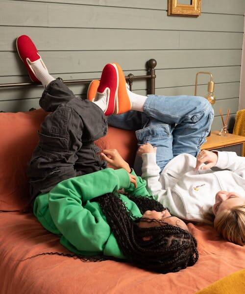 Deux femmes allongées sur un lit portant des charentaises rouge et orange fabriquées en France par Esperluette.