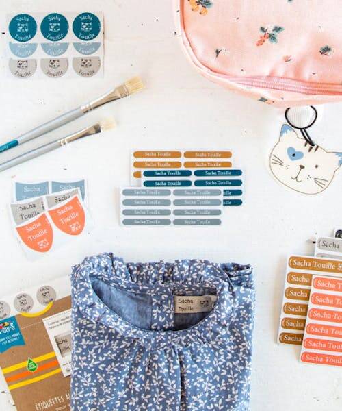 Photo exposant des étiquettes de marquage fabriquées en France par A-qui-S pour vêtements et fournitures scolaires.