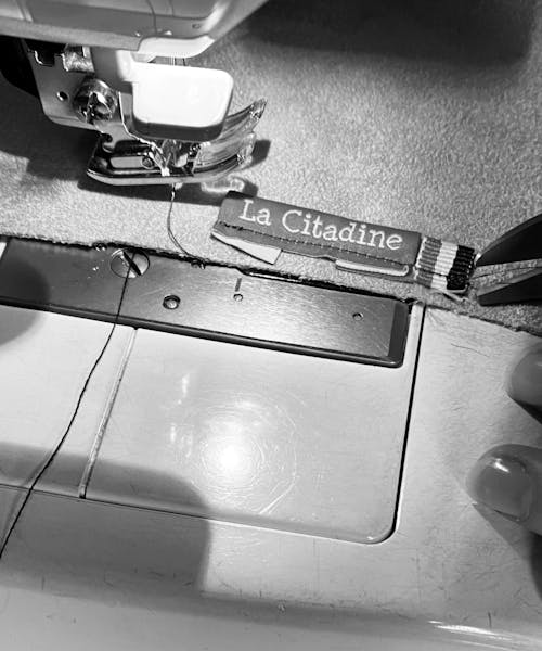 Photo d'une couturière en train de coudre une étiquette La Citadine sur un sac fabriqué en France.