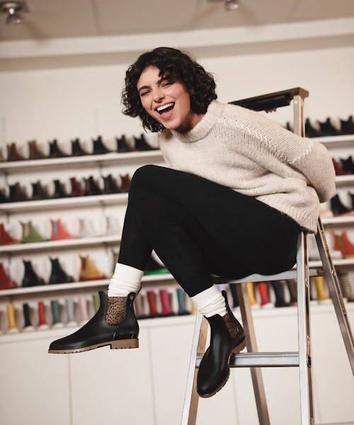 Femme brune assise sur un tabouret portant des bottines Méduse Made in France.
