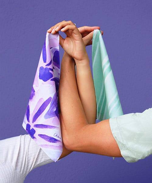 Deux bras entrecroisés portent un mouchoir Made in France vert et un mouchoir français violet avec motifs.