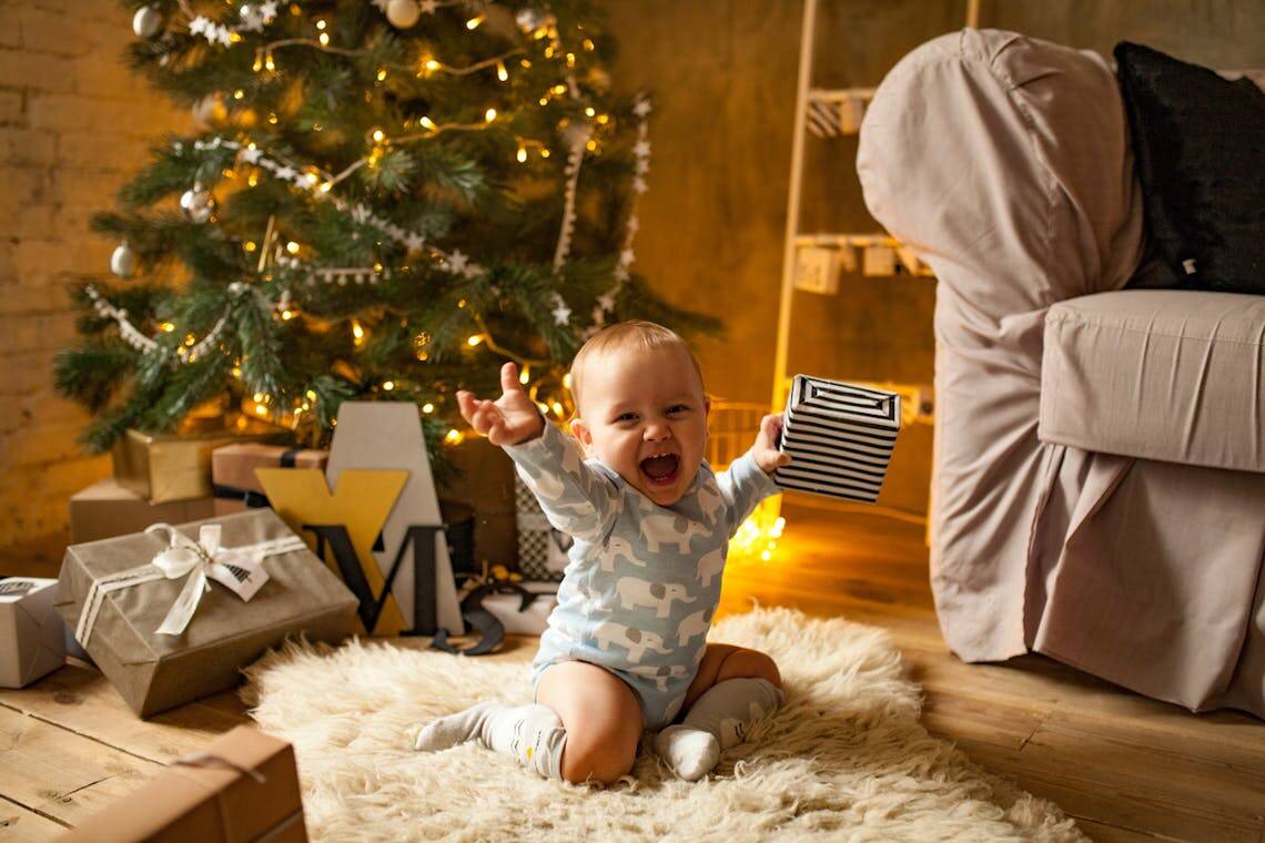 Bébé découvrant avec joie son cadeau made in France près du sapin de Noël. 