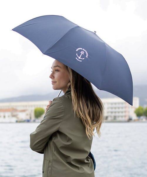 Femme portant un parapluie bleu fabriqué en France par Le Parapluie de Cherbourg en collaboration avec la marine nationale.