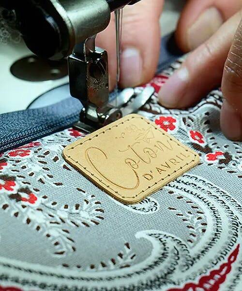 Couturière en train de broder un écusson sur un sac fabriqué en France par Coton d'Avril.