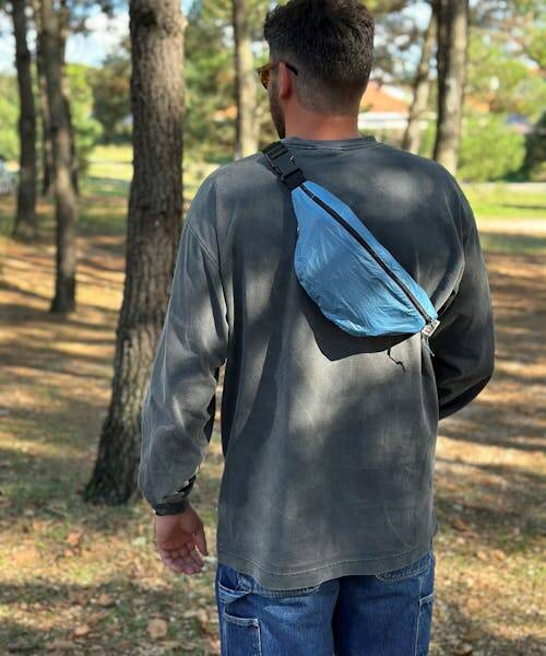 Homme se baladant dans la forêt en portant en bandoulière un sac banane upcyclé français de la marque NKIUP. 