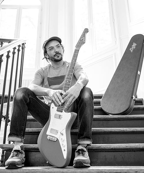 Guitariste assis tenant une guitare électrique fabriquée en France par Berg. Copyright photo : Richard Storchi.
