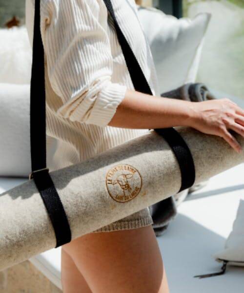Femme portant un tapis de yoga fabriqué en France par Le Tapis de Laine en bandoulière. 