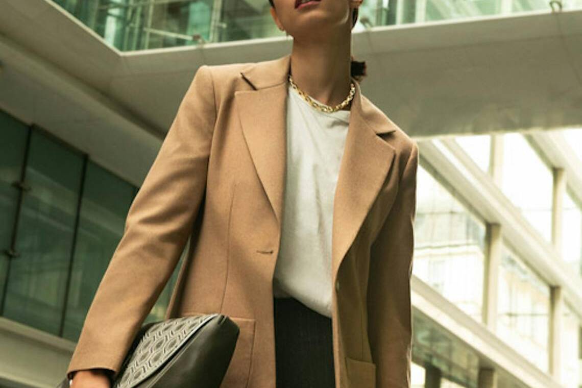 Femme portant une veste beige Made in France avec un jean noir et une sacoche.