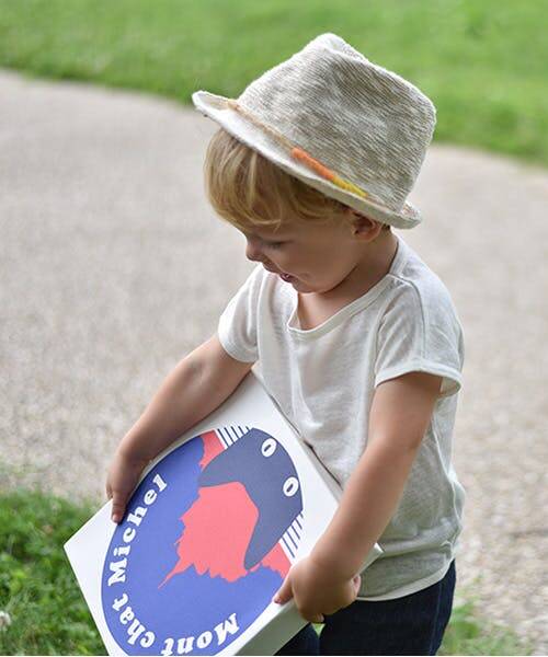 Petit garçon blond portant un chapeau ainsi qu'un t-shirt blanc et un jean bleu en lin.