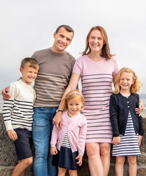 Famille avec leurs trois enfants portant pulls marins, gilet et robe fabriqués en France.