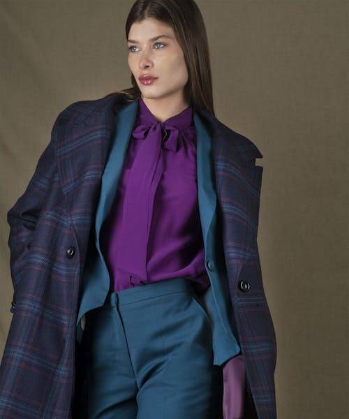 Femme brune portant un tailleur fabriqué en France par My Tailor is Joh bleu, accompagné d'un chemisier violet et d'un manteau. 